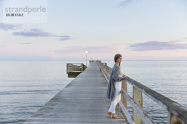 Frau auf Pier mit Blick aufs Meer