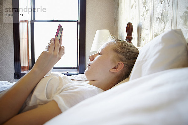Junge Frau im Bett mit Mobiltelefon