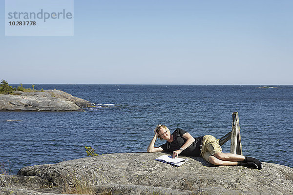 Frau mit Buch auf einem Felsen am Meer