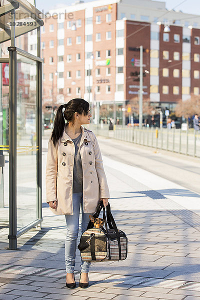 Frau an Straßenbahnhaltestelle mit Hund in Tasche