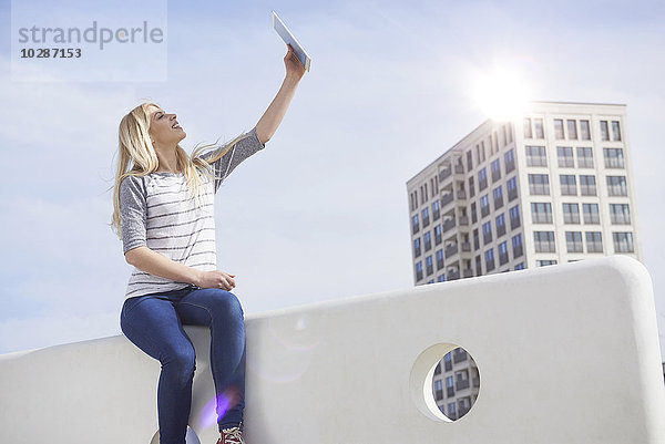 Teenager-Mädchen sitzt auf einer Mauer und macht ein Selfie mit digitalem Tablet  München  Bayern  Deutschland