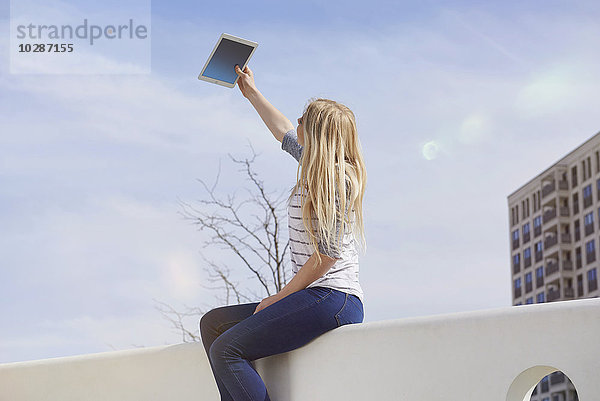 Teenager-Mädchen sitzt auf einer Mauer und macht ein Selfie mit digitalem Tablet  München  Bayern  Deutschland