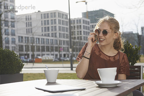 Junge Frau spricht in einem Straßencafé mit einem Mobiltelefon  München  Bayern  Deutschland