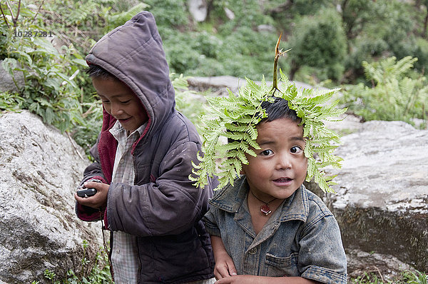 Junge spielt mit Mobiltelefon und ein anderer mit Farnblatt  Nepal