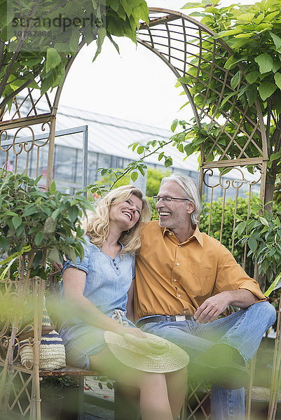 Älteres Paar sitzt auf einer Bank und lächelt in einer Gärtnerei  Augsburg  Bayern  Deutschland