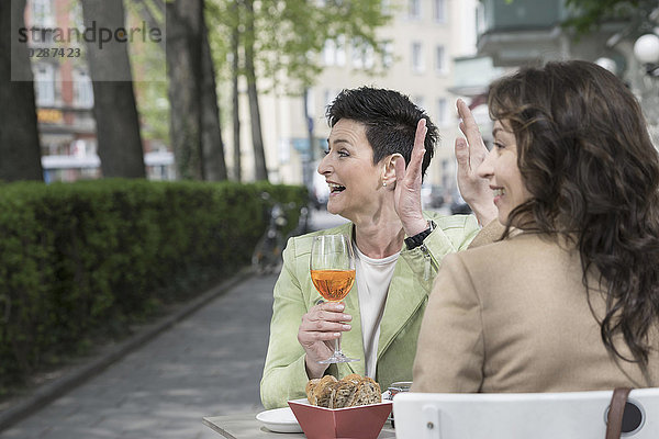 Zwei Freunde winken sich in einem Straßencafé zu  Bayern  Deutschland