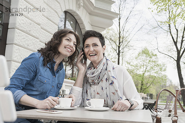 Zwei Freunde im Straßencafé und beim Telefonieren  Bayern  Deutschland