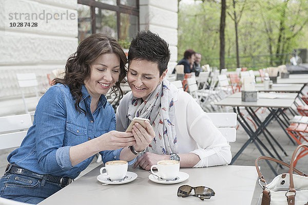 Zwei Freunde im Straßencafé schauen auf das Telefon  Bayern  Deutschland