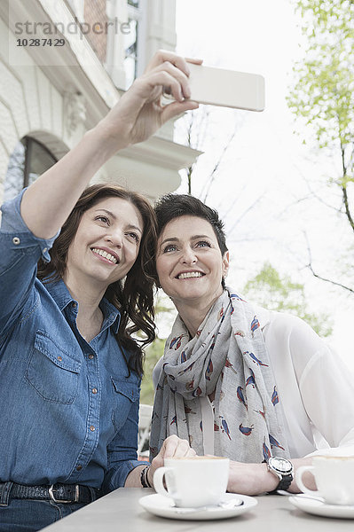 Zwei Freunde machen ein Selfie in einem Straßencafé  Bayern  Deutschland