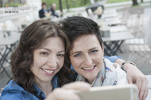 Zwei Freunde machen ein Selfie in einem Straßencafé  Bayern  Deutschland