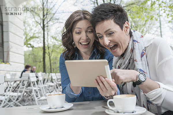 Zwei Freunde benutzen ein digitales Tablet in einem Straßencafé  Bayern  Deutschland