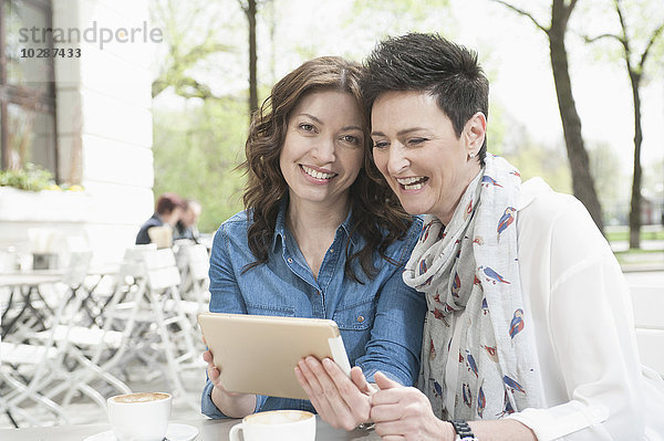 Zwei Freunde benutzen ein digitales Tablet in einem Straßencafé  Bayern  Deutschland