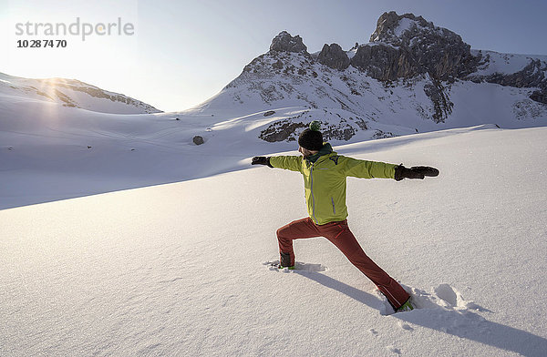 Mann beim Yoga auf schneebedecktem Berg bei Sonnenaufgang  Tirol  Österreich