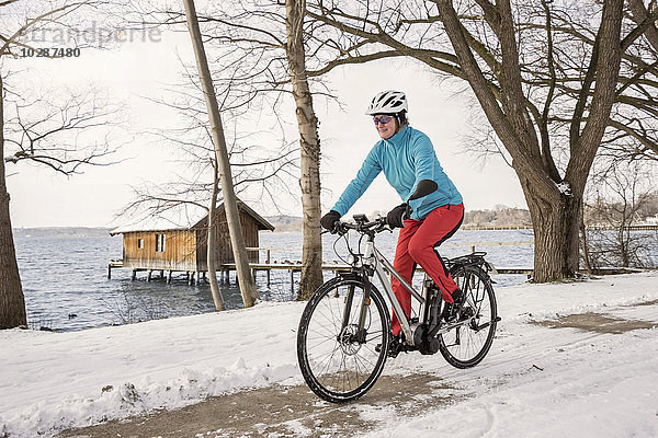 Ältere Frau fährt Fahrrad auf schneebedeckter Straße  Bayern  Deutschland