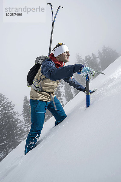 Männlicher Bergsteiger  der mit einer Pickelaxt einen verschneiten Hang hinaufsteigt  Zell am See  Österreich