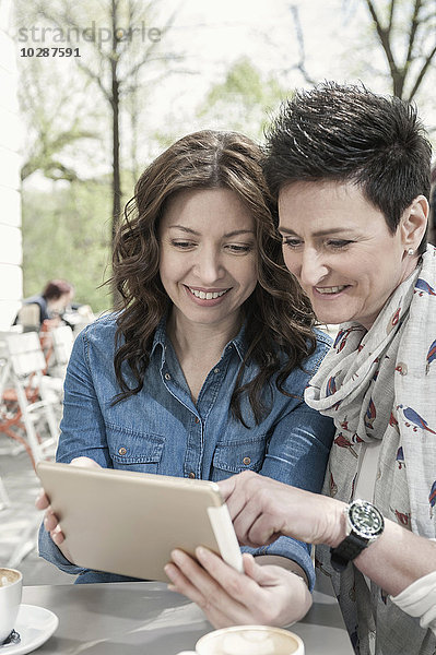 Zwei Freunde benutzen ein digitales Tablet in einem Straßencafé  Bayern  Deutschland