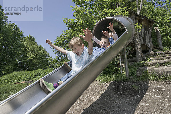 Drei Freunde rutschen auf einer Rutsche auf einem Spielplatz  München  Bayern  Deutschland