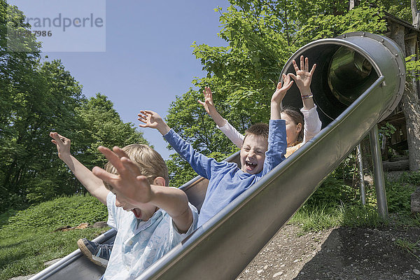 Drei Freunde rutschen auf einer Rutsche auf einem Spielplatz  München  Bayern  Deutschland