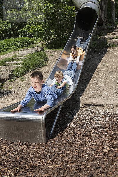 Drei Freunde rutschen auf einer Röhrenrutsche auf einem Spielplatz hinunter  München  Bayern  Deutschland