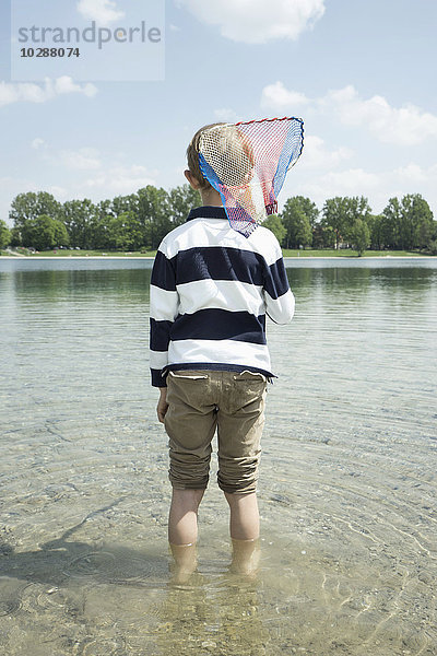 Rückansicht eines Jungen  der einen Brailer in den See hält  Bayern  Deutschland