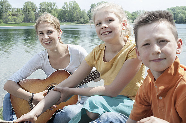 Junge Anführerin spielt Gitarre mit ihren Freunden am See  Bayern  Deutschland