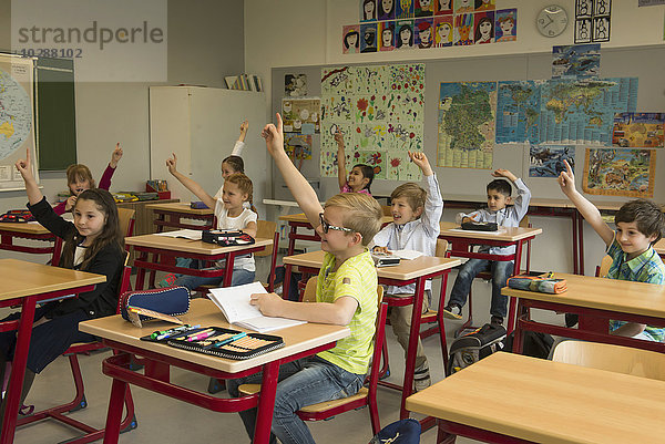 Schulkinder mit erhobenen Händen im Klassenzimmer  München  Bayern  Deutschland