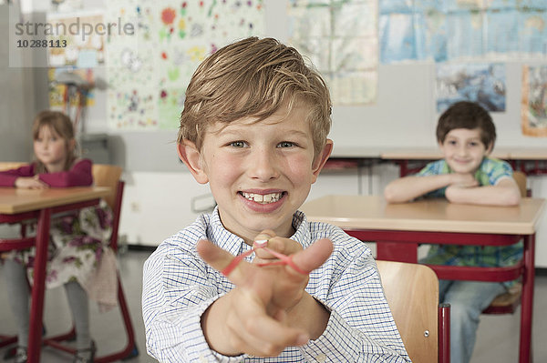 Schuljunge mit einer Steinschleuder und lächelnd im Klassenzimmer  München  Bayern  Deutschland