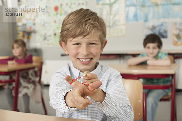 Schuljunge mit einer Steinschleuder und lächelnd im Klassenzimmer  München  Bayern  Deutschland