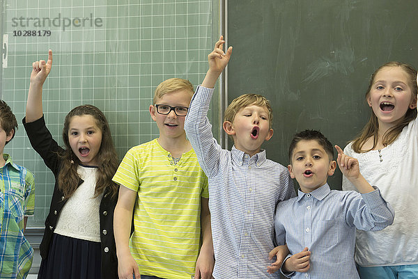 Schüler heben die Hände vor der Tafel in einem Klassenzimmer  München  Bayern  Deutschland