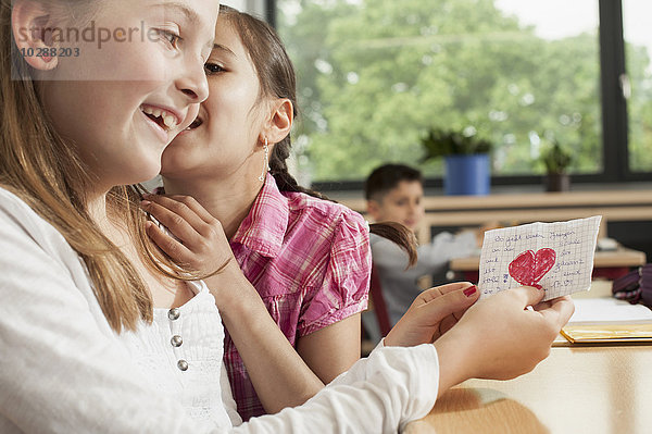 Schulmädchen flüstern im Klassenzimmer und zeigen einen Liebesbrief  München  Bayern  Deutschland