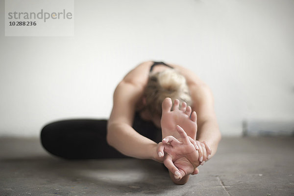 Mittlere erwachsene Frau beim Üben der Janu-Sirsasana-Pose im Yogastudio  München  Bayern  Deutschland