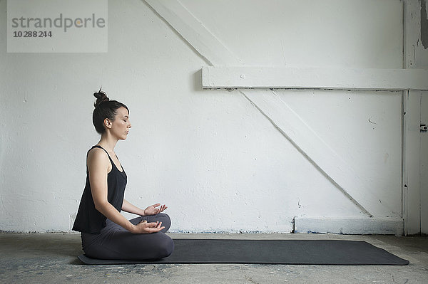 Seitenprofil einer mittelgroßen erwachsenen Frau  die in einem Yogastudio den Lotussitz übt  München  Bayern  Deutschland
