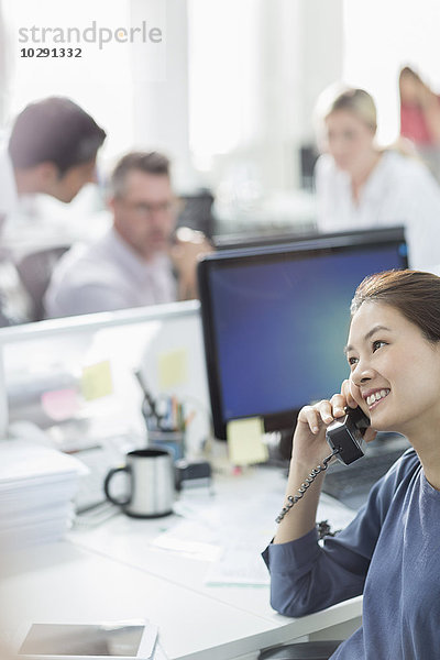 Lächelnde Geschäftsfrau beim Telefonieren am Schreibtisch im Büro