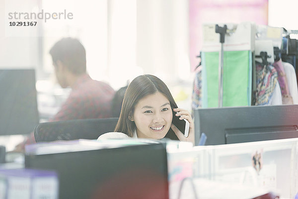 Lächelnde Modedesignerin beim Telefonieren am Schreibtisch im Büro