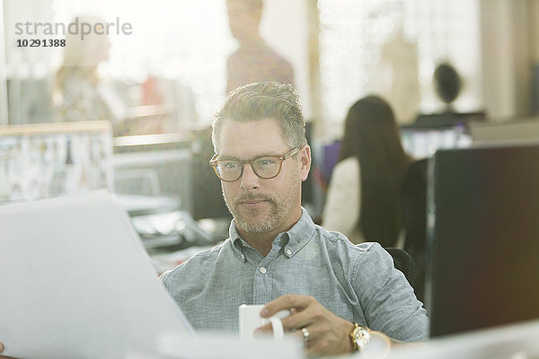 Modedesignerin bei der Überprüfung von Papierkram und Kaffeetrinken im Büro