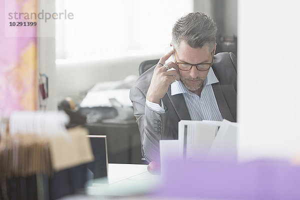 Fokussierter Geschäftsmann  der den Papierkram am Schreibtisch im Büro überprüft.