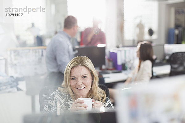 Portrait lächelnder Modedesigner beim Kaffeetrinken am Computer im Büro