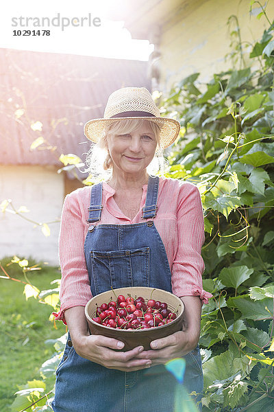 Portrait lächelnde Frau im Overall mit geernteten Kirschen