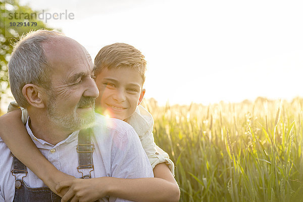 Portrait liebevoller Enkel umarmender Großvater im ländlichen Weizenfeld