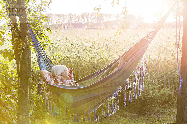 Gelassene Frau schläft in der Hängematte neben dem sonnigen  ländlichen Weizenfeld.