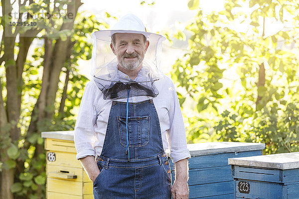 Porträt selbstbewusster Imker in Schutzhut neben Bienenstöcken