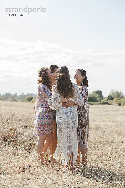 Boho-Frauen umarmen sich im Kreis im sonnigen ländlichen Feld