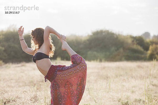 Boho Frau in König Tänzerin Yoga Pose im sonnigen ländlichen Bereich