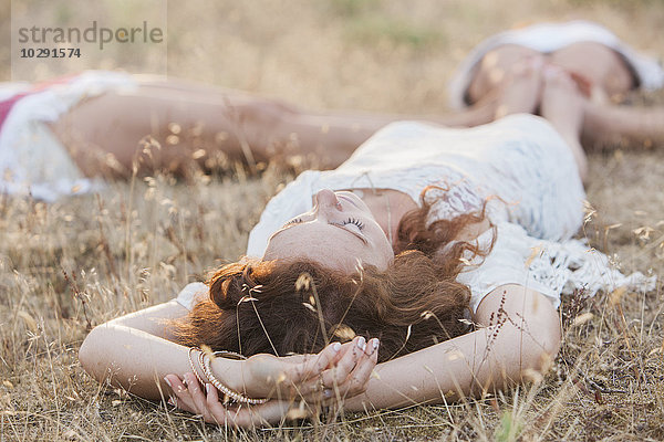 Boho-Frauen  die im Kreis liegen und die Füße auf dem Land berühren.