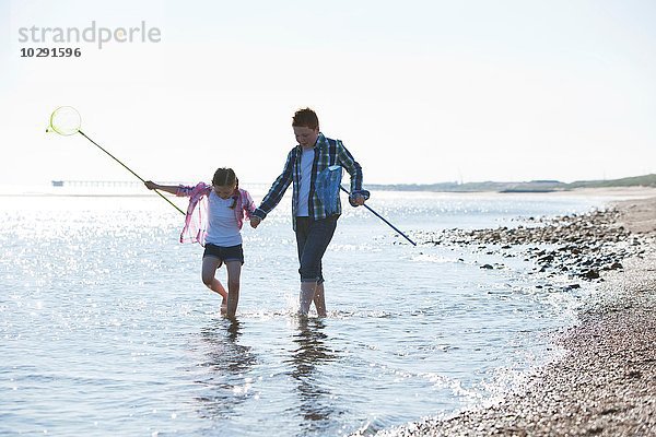 Mädchen und Junge paddeln im Wasser  halten sich an den Händen  tragen Fischernetze und schauen nach unten.