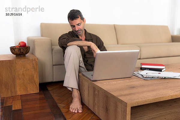 Barfuss reifer Mann auf Holzboden sitzend mit Laptop  Blick nach unten