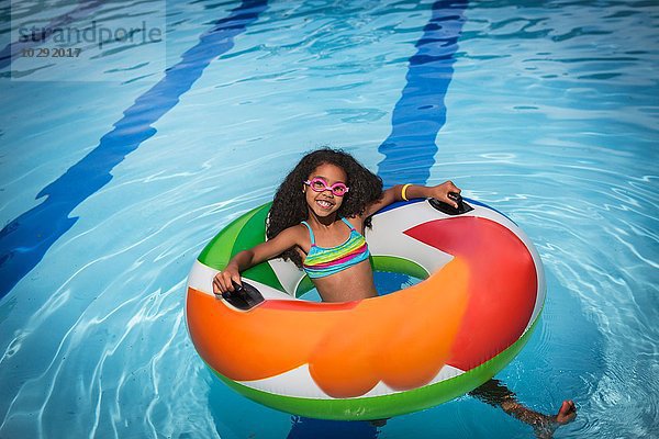 Mädchen sitzt im aufblasbaren Ring im Schwimmbad und schaut lächelnd auf die Kamera.