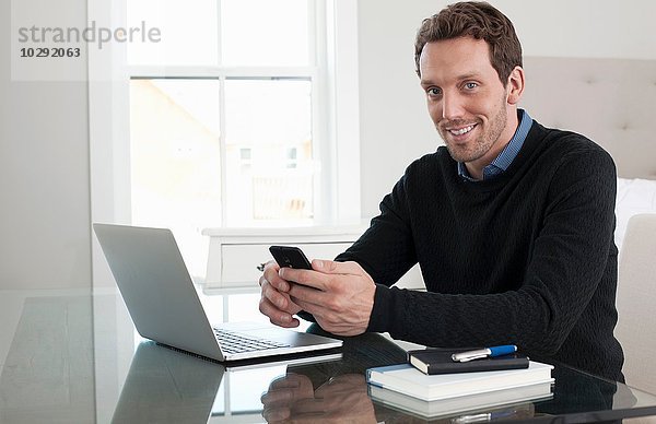 Mittlerer Erwachsener Mann am Tisch sitzend  mit Laptop und Smartphone