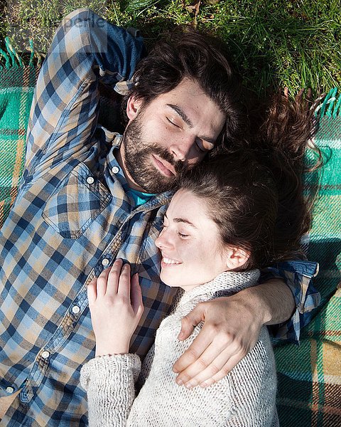 Draufsicht auf das junge Paar mit geschlossenen Augen auf Picknickdecke