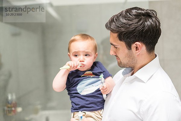 Vater hält jungen Sohn  während der Sohn die Zähne putzt.